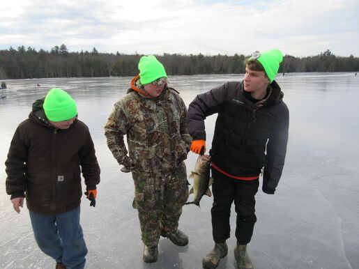 Three scouts holding a fish on a frozen lake